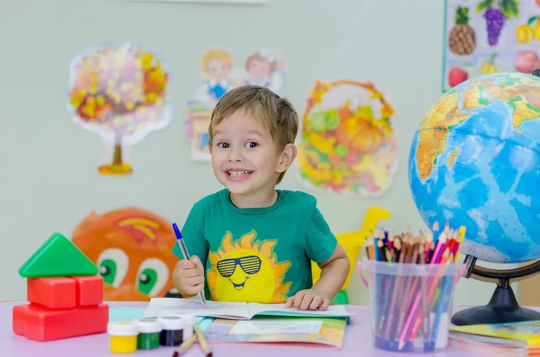 Boy smiling at a school desk with colorful supplies