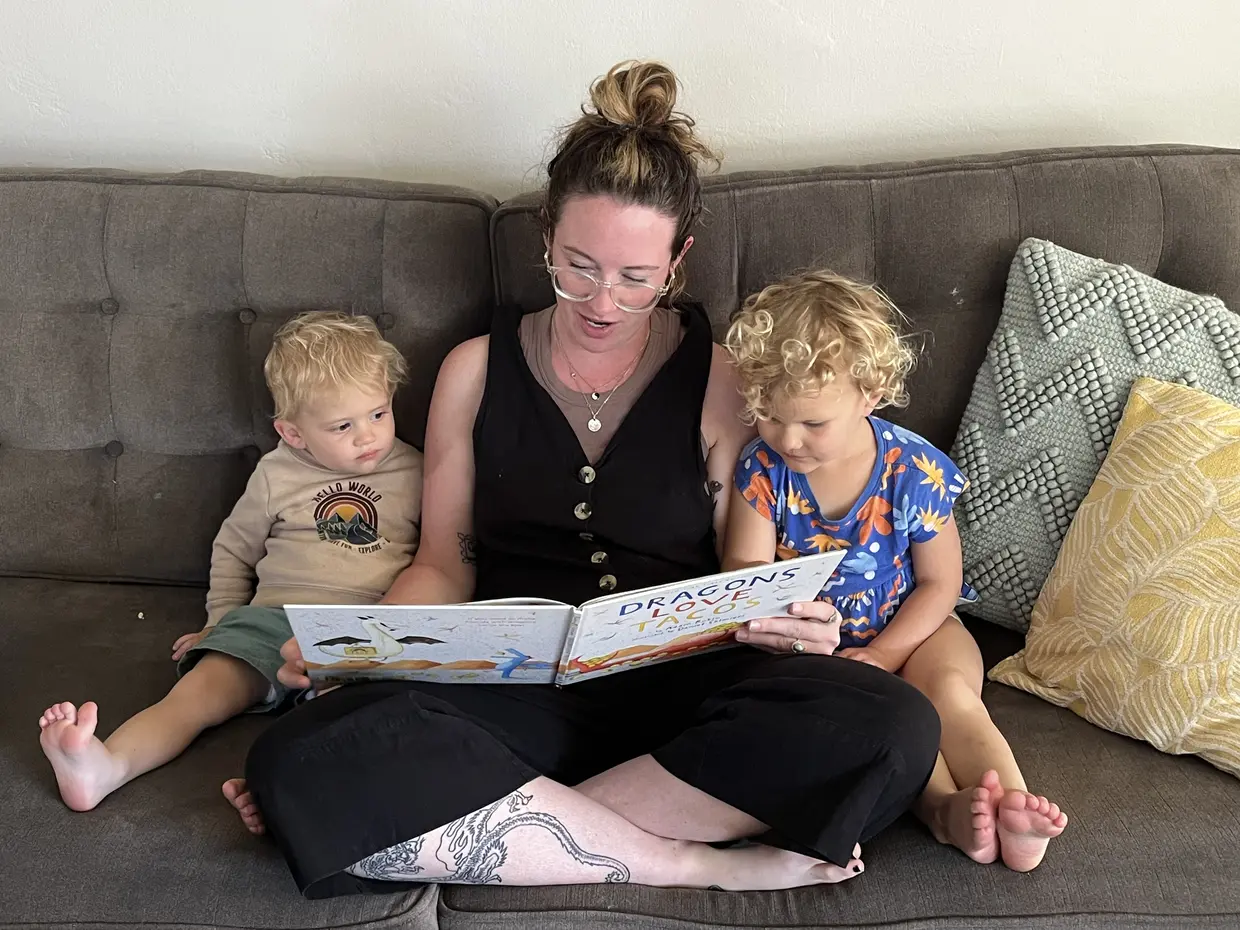 Speech therapist reading Dragons Love Tacos to two toddlers on a couch