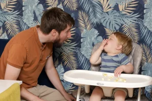 Toddler clapping with delight during a play-based therapy session with two speech therapists